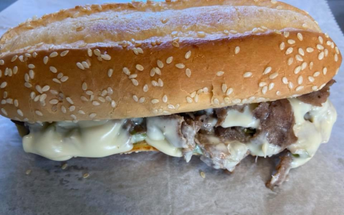 A sesame seed bun filled with sliced meat and creamy sauce, resting on a piece of parchment paper.