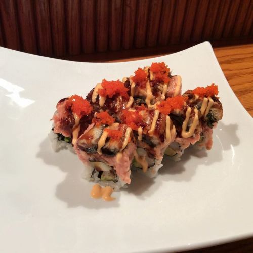 A plate of sushi rolls topped with orange fish roe and drizzled with sauce, served on a white dish.