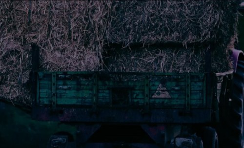 A green trailer loaded with hay bales, set against a dark background.