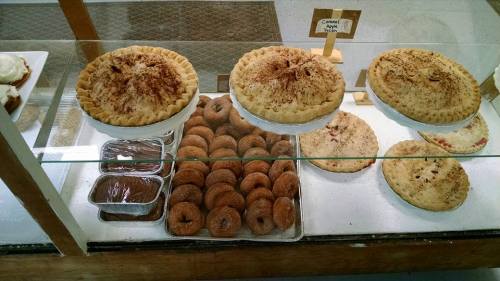 Display case with three pies and a tray of assorted donuts, showcasing a variety of baked goods.