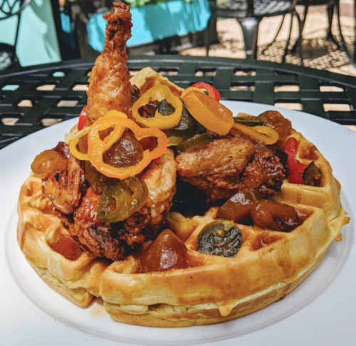 A plate of waffles topped with fried chicken, pickled peppers, and a drizzle of sauce.