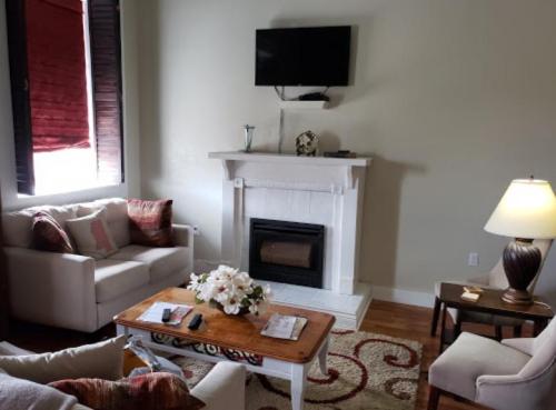 Cozy living room with a fireplace, TV, white sofas, a wooden coffee table, and a lamp, decorated with flowers.