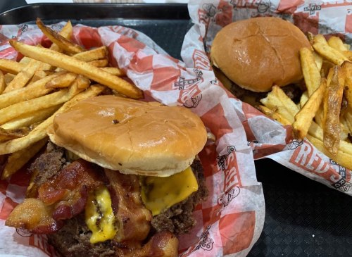 Two burgers with cheese and bacon on buns, served with a side of golden French fries in red and white paper.