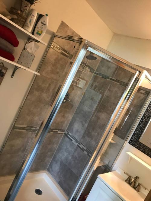A modern bathroom featuring a glass shower enclosure, tiled walls, and a white vanity with toiletries on the counter.