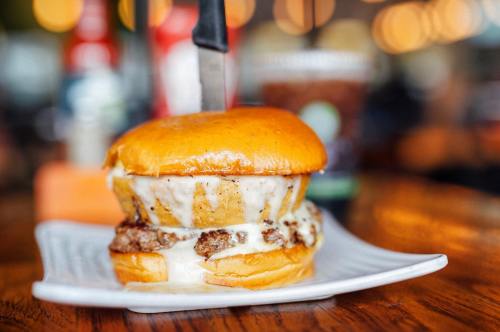 A juicy burger with melted cheese and a knife inserted, served on a plate with a blurred background.