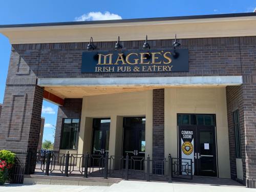 Exterior of Magee's Irish Pub & Eatery, featuring a sign and a "Coming Soon" notice on the door. Bright blue sky above.
