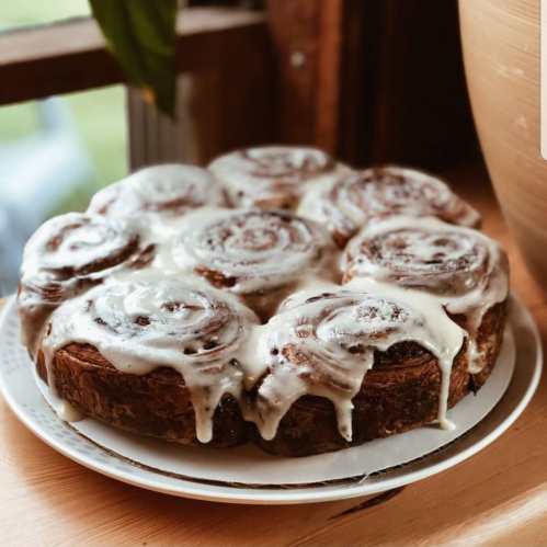 A plate of freshly baked cinnamon rolls topped with creamy icing, sitting by a window.
