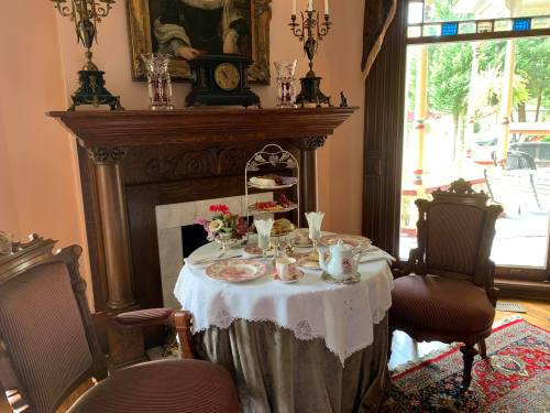 A beautifully set tea table with fine china, pastries, and a decorative fireplace in an elegant room.