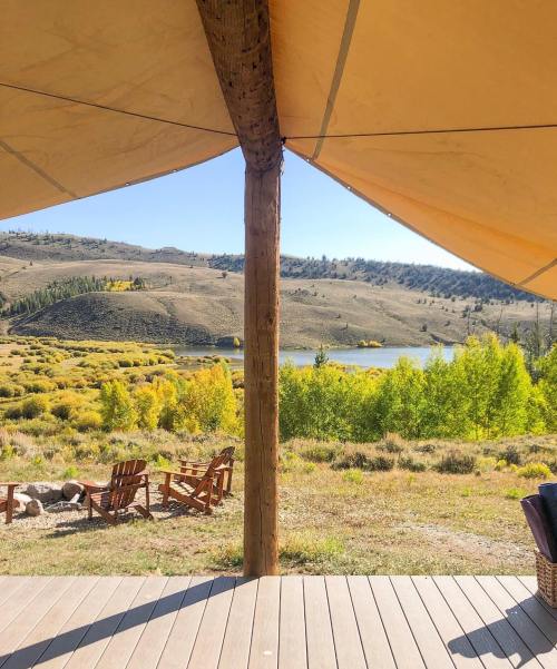 View from a tent porch overlooking a serene lake surrounded by hills and colorful autumn foliage.