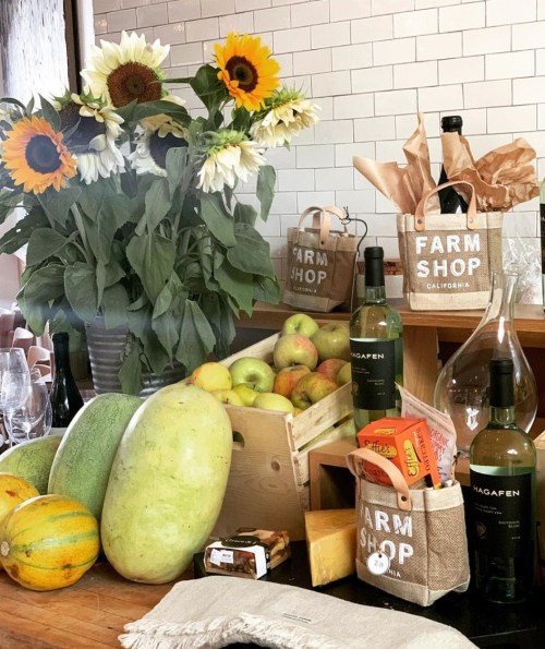 A rustic display of fresh produce, wine bottles, and sunflowers in a farm shop setting.