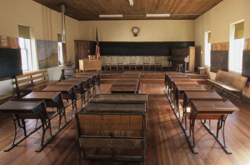 A vintage classroom with wooden desks, a chalkboard, and a clock, featuring a warm, rustic atmosphere.