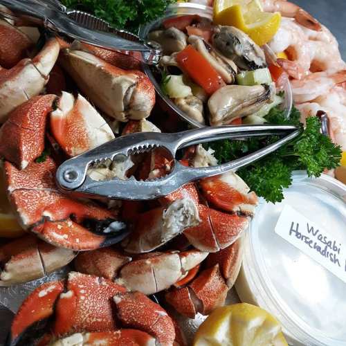 A close-up of seafood, including crab claws, shrimp, and mussels, with garnishes and wasabi horseradish on the side.