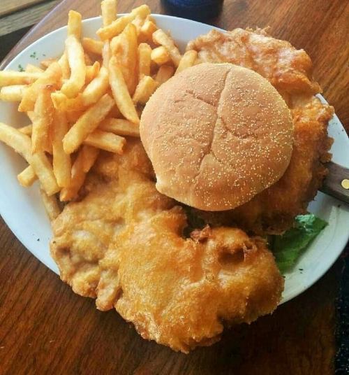 A plate of crispy fried chicken, a bun, and golden French fries on a wooden table.