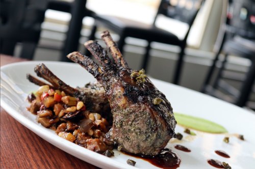 A plate featuring grilled lamb chops with a side of sautéed vegetables and a drizzle of sauce.