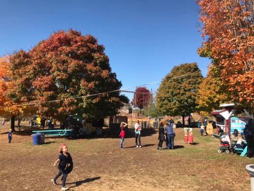A vibrant park scene with colorful autumn trees, children playing, and families enjoying the outdoors on a sunny day.