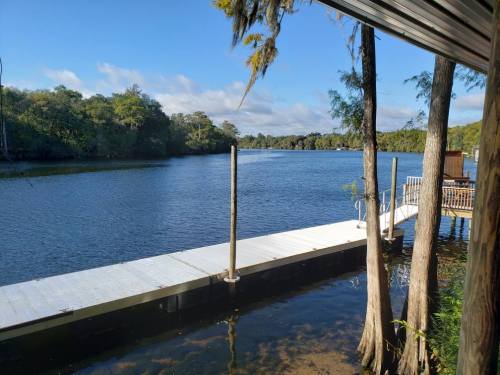 A serene river view with a wooden dock, surrounded by lush greenery and a clear blue sky.