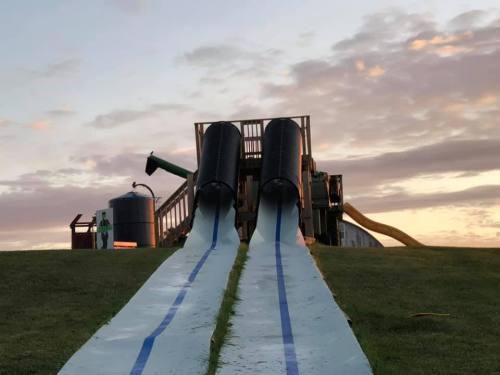Two large water slides descend from a wooden structure, set against a sunset sky with clouds.