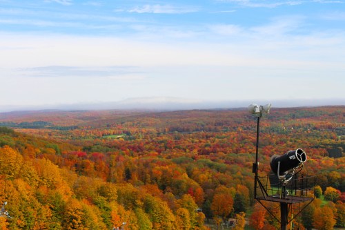 A scenic view of vibrant autumn foliage across rolling hills, with a ski tower in the foreground against a clear blue sky.
