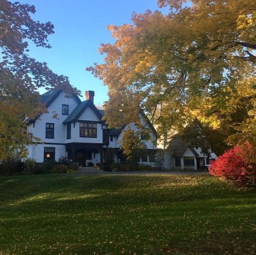 A large, charming house surrounded by vibrant autumn trees and colorful foliage under a clear blue sky.