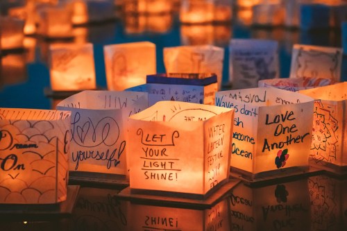 Illuminated paper lanterns with handwritten messages float on water, creating a serene and hopeful atmosphere.