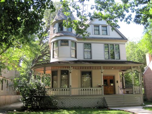 A charming Victorian-style house with a turret, surrounded by trees and a well-maintained lawn.