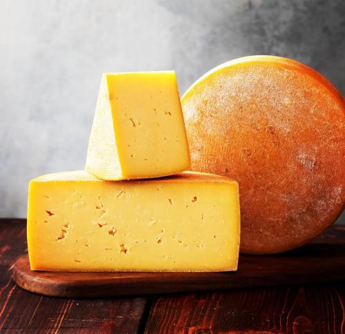 A wooden board with three pieces of yellow cheese, including a wedge and a round wheel, against a textured background.