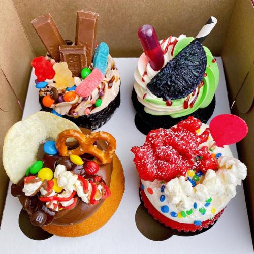 Colorful cupcakes topped with various candies and treats, arranged in a box.