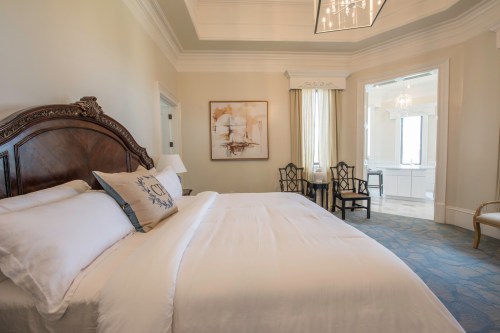 A spacious, elegantly decorated bedroom with a large bed, artwork, and a seating area by a window.