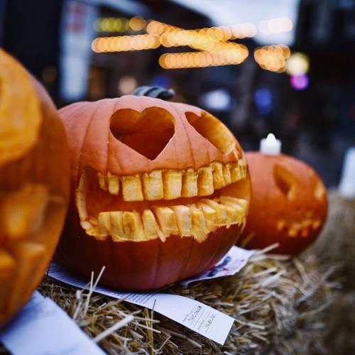 Three carved pumpkins with unique designs, featuring a heart and a toothy grin, displayed on hay bales.