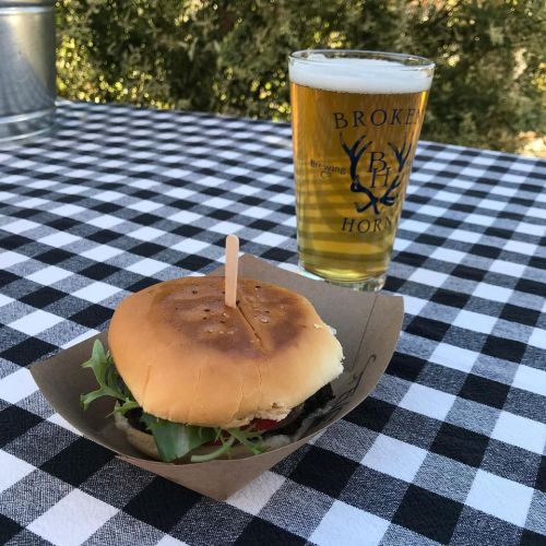 A burger with lettuce on a paper tray next to a glass of beer, set on a black and white checkered tablecloth.