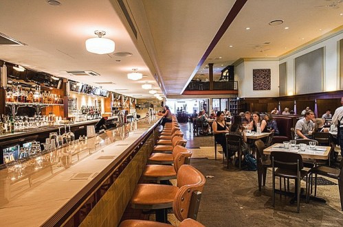 A spacious bar with a long counter, seating, and patrons dining in a lively restaurant atmosphere.