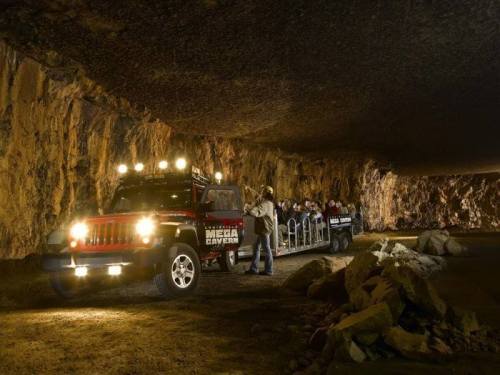 A tour group boards a jeep inside a cavern, surrounded by rocky walls and dim lighting.
