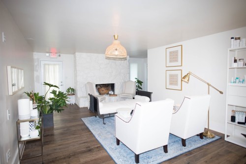 A cozy, modern waiting area with white chairs, a blue rug, plants, and a decorative light fixture.