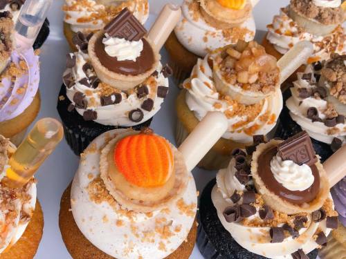A variety of decorated cupcakes with colorful frosting, toppings, and unique garnishes like candies and chocolate pieces.