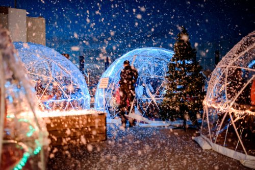 A snowy scene featuring illuminated igloo-like structures and a person walking among them on a rooftop.
