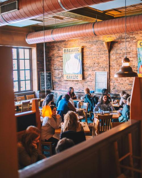 A cozy restaurant interior with wooden tables, patrons dining, and a brick wall adorned with organic garlic signage.