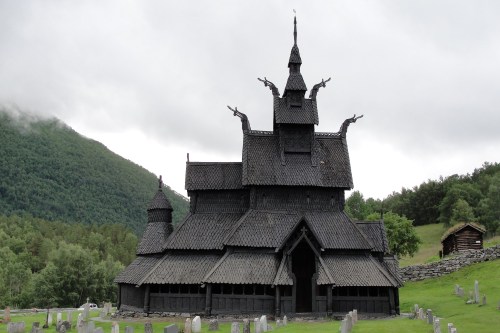 A striking black wooden church with intricate architecture, surrounded by green hills and a graveyard in the foreground.