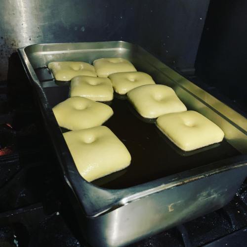 A metal tray filled with dough squares frying in oil on a stovetop.