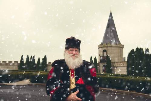 A snowy scene featuring Santa Claus in a red and black outfit, with a castle tower in the background.