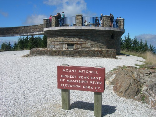 A stone observation tower at Mount Mitchell, with visitors and a sign indicating it's the highest peak east of the Mississippi.