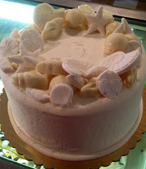 A round cake decorated with white chocolate seashells and starfish on top, set on a gold base.