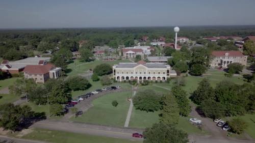 Aerial view of a college campus with buildings, trees, and a water tower in the background.