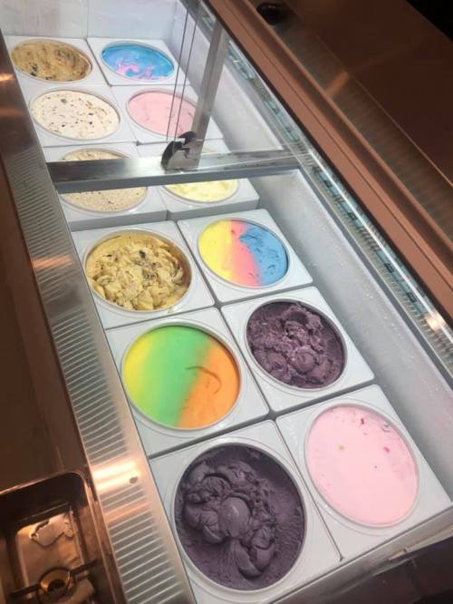 A display of various colorful ice cream flavors in a freezer, including purple, blue, yellow, and rainbow swirls.