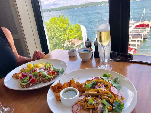 Two plates of colorful tacos and a salad, with a glass of champagne, overlooking a scenic waterfront view.