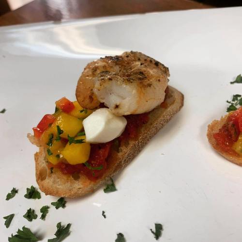 A toasted bread slice topped with shrimp, mango salsa, and a dollop of cheese, garnished with parsley.