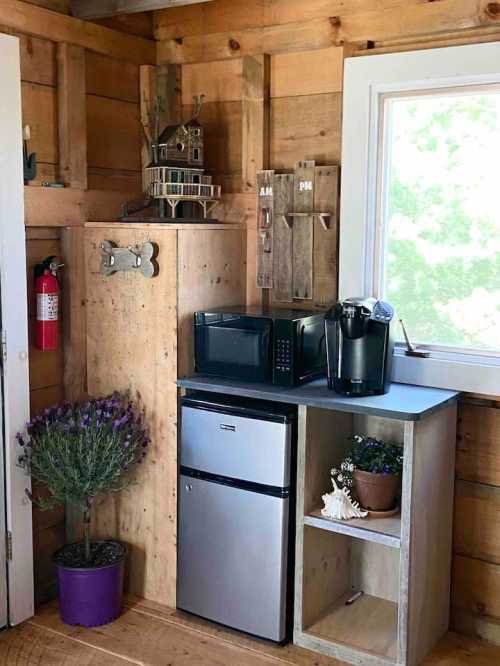 Cozy corner with a microwave, mini fridge, coffee maker, and decorative items in a wooden cabin interior.