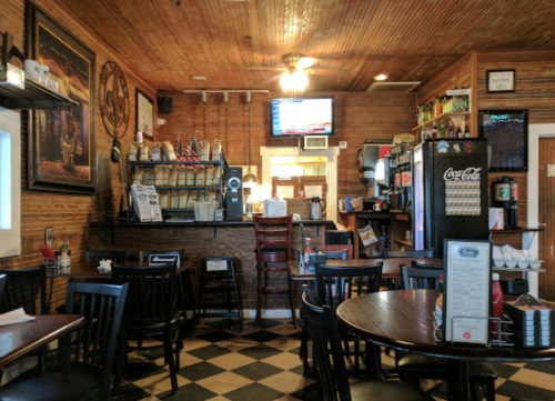 Cozy restaurant interior with wooden decor, a bar area, and checkered floor, featuring tables and a TV in the background.