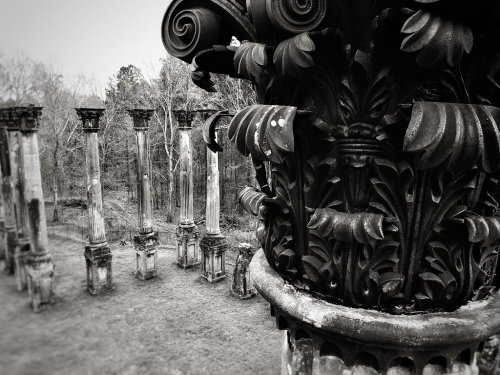 Close-up of an ornate column with intricate designs, overlooking a row of weathered stone pillars in a misty landscape.