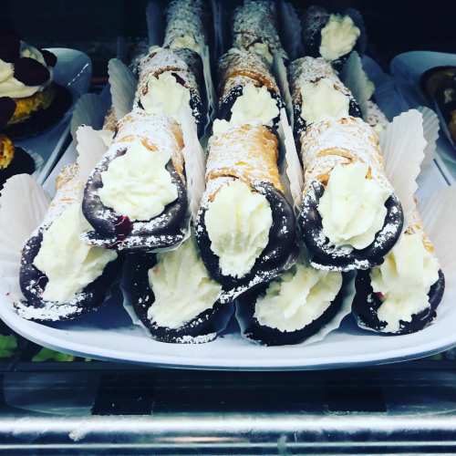 A display of cannoli filled with cream, dusted with powdered sugar, and dipped in chocolate.