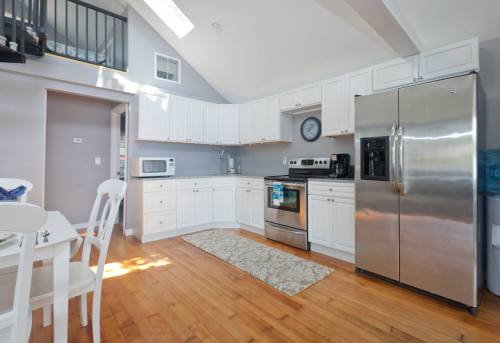 Bright kitchen with white cabinets, stainless steel appliances, and wooden flooring, featuring a dining area.